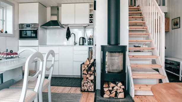 A modern kitchen with white cabinets, a built-in oven, and a stove. There is a dining area with a white table and chairs. A staircase with wooden steps leads to a lofted area. - Cozy home in Södra Vi with sauna (Södra Vi)