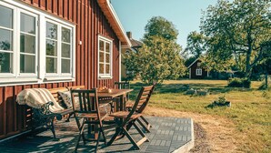 A wooden house with a patio table and chairs, surrounded by a grassy yard and trees. - Cozy home in Södra Vi with sauna (Södra Vi)