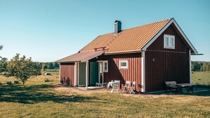 A red barn with a sloped roof, a green door, and a small porch with white chairs and a table. - Cozy home in Södra Vi with sauna (Södra Vi)
