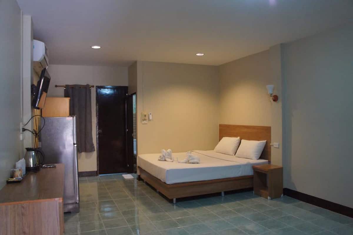 A hotel room with a bed, bedside table, lamp, and a door leading to another room.
