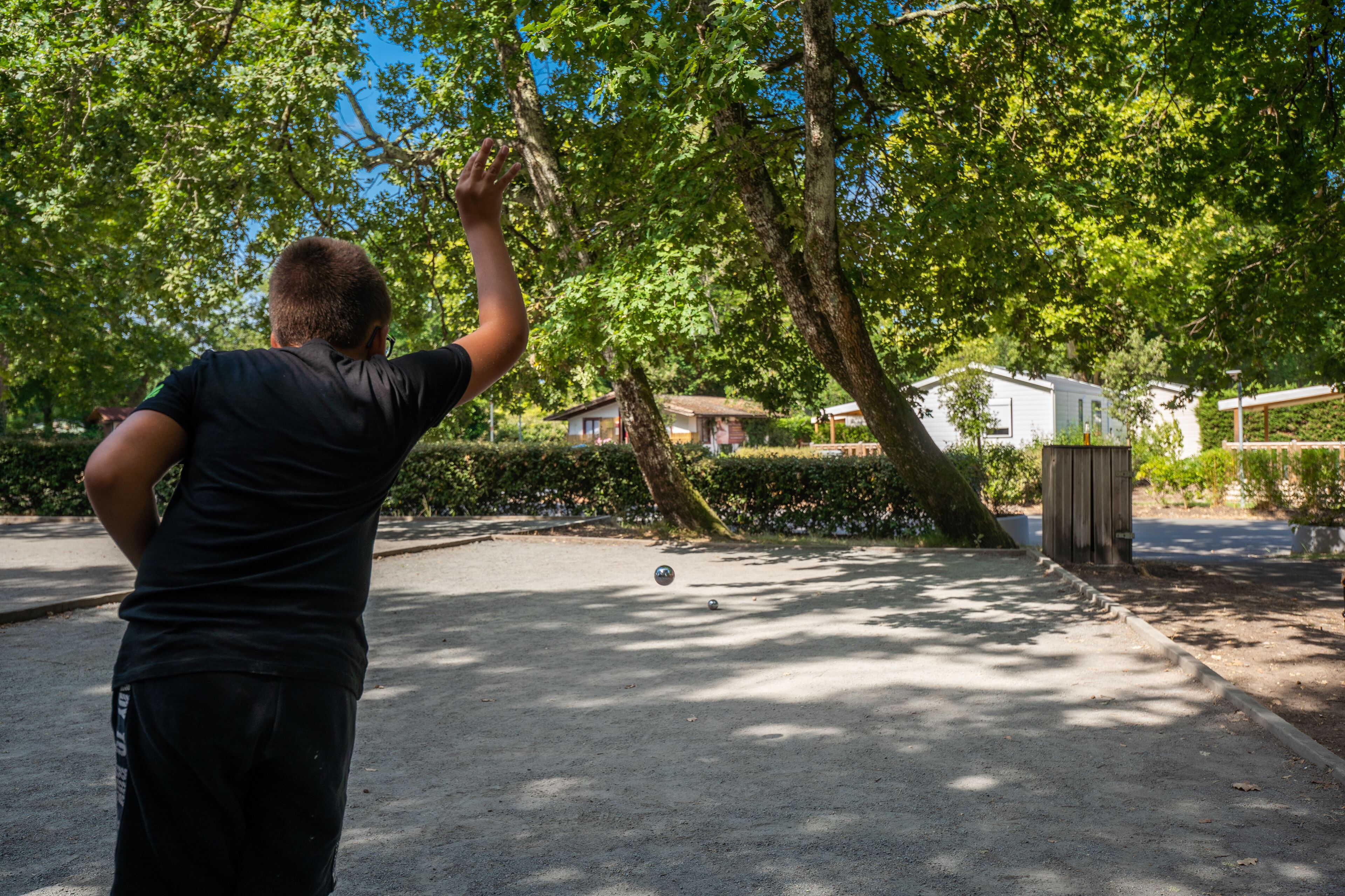 A person playing with a ball in a park with trees and a house in the background.