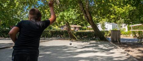 A person playing with a ball in a park with trees and a house in the background.