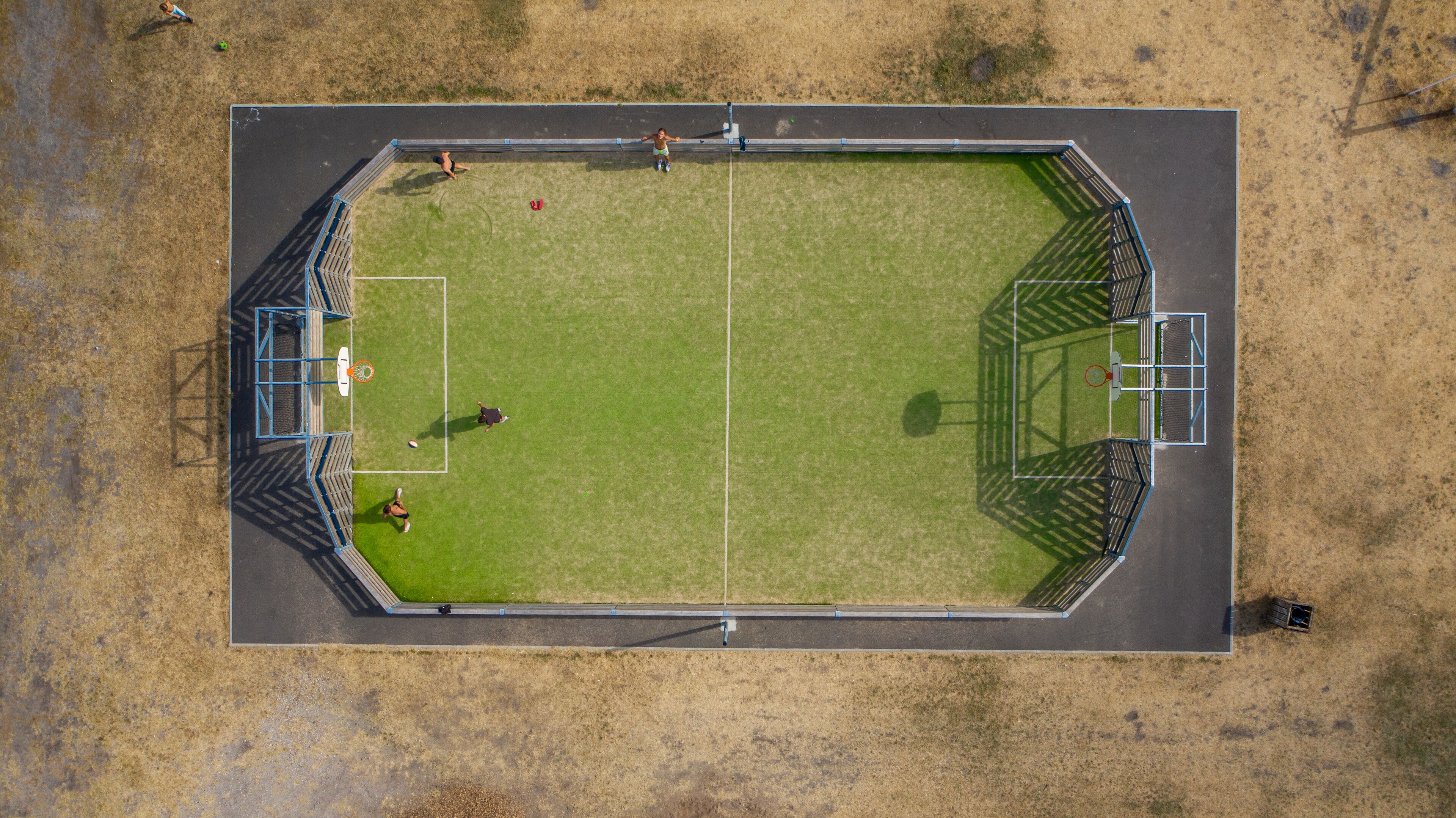 Vue aérienne d’un terrain de sport rectangulaire, avec des poteaux de but, une piste d’athlétisme et des gradins pour les spectateurs.