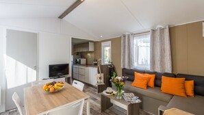 Una sala de estar moderna con un sofá, una mesa de comedor con fruta, un televisor y una zona de cocina.