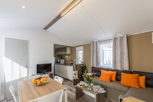 Una sala de estar moderna con un sofá, una mesa de comedor con fruta, un televisor y una zona de cocina.