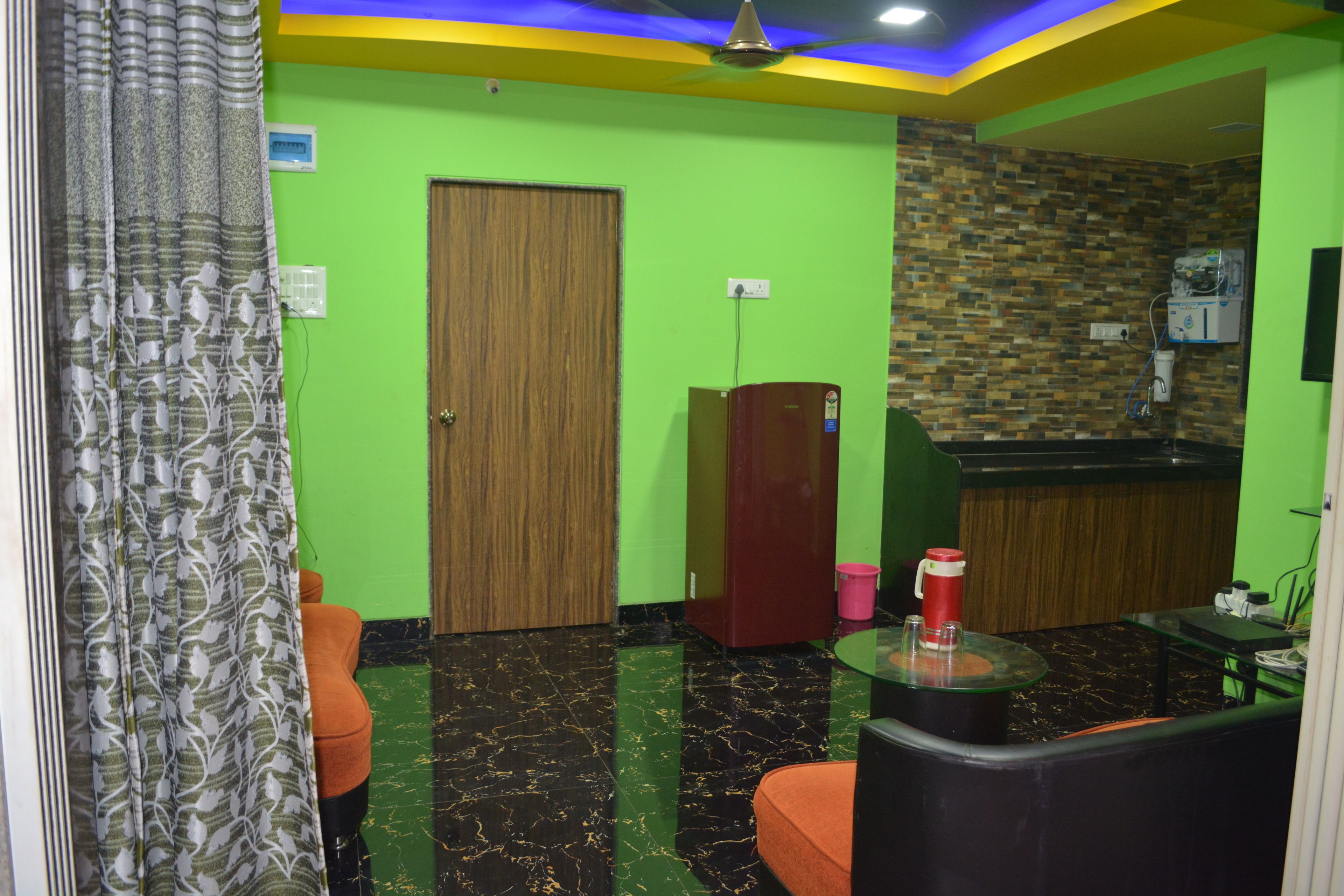 A room with a wooden door, a refrigerator, a small table with a red cup, and a patterned curtain.