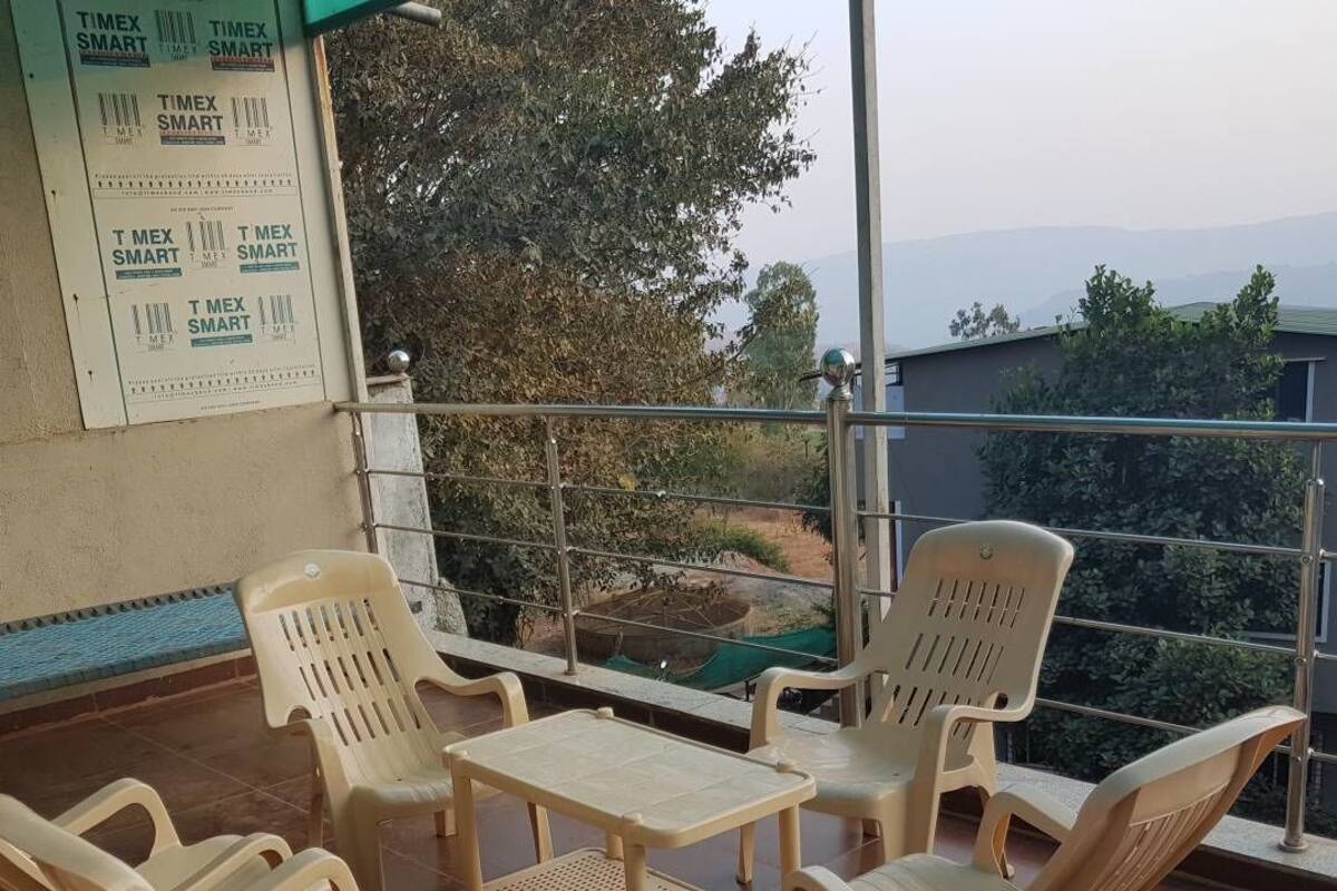 Un balcón con sillas de plástico y una mesita, con vistas a un jardín y colinas lejanas.