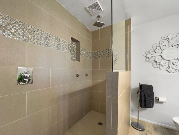 Casa de banho moderna com azulejos bege, cabine de duche em vidro, sanita com barra para toalhas e um elemento decorativo na parede.