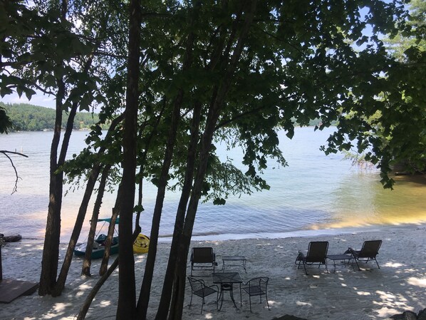 A beach with a table and chairs, a boat, and trees.