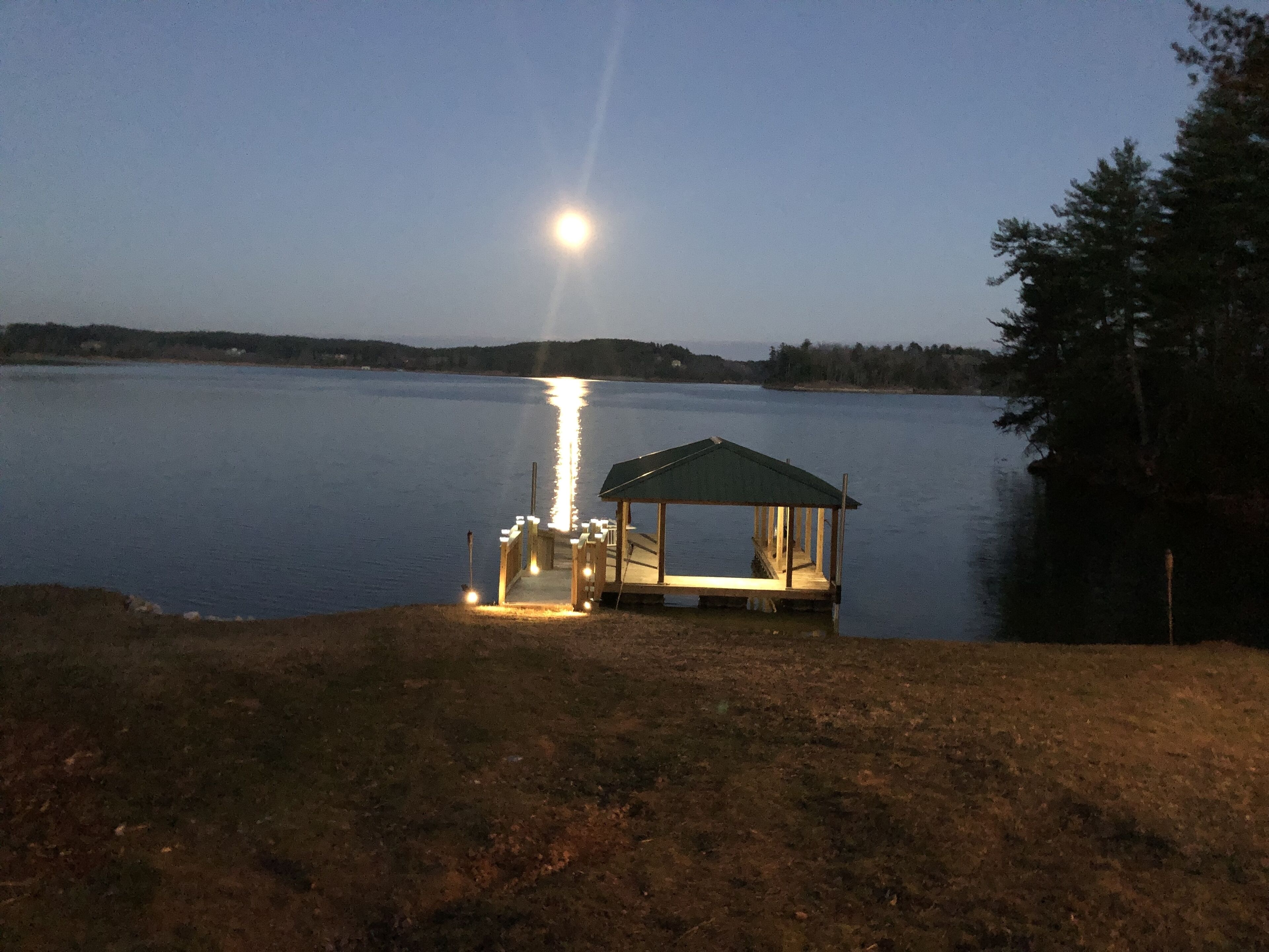 Une jetée dotée d’un espace de repos abrité et d’un petit abri, offrant une vue sur un lac paisible où se reflète la lune.
