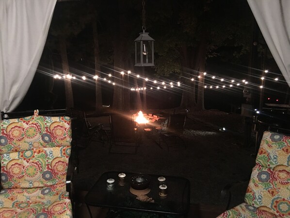 Un espacio al aire libre con mesa y sillas, luces de cadena y un farol.