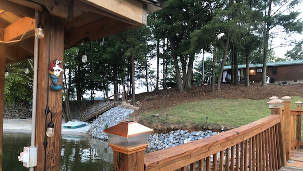 A wooden deck with a railing overlooking a body of water, surrounded by trees and a stone wall.