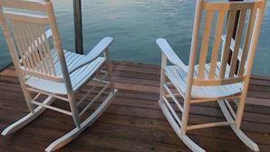 Two rocking chairs on a wooden deck overlooking a calm lake with a distant shoreline.