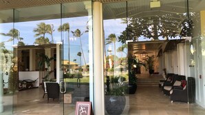 A hotel entrance with a wet floor sign, glass doors, and a view of palm trees and a pool. - Deluxe Room w/King Bd, Ocean/Pool views, New Furnishings!, No Resort Fee (Lihue)