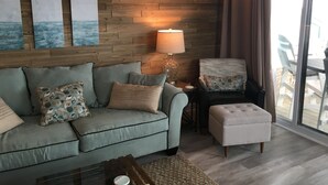 A living room with a wooden wall, a sofa, a chair, a table, and a lamp. - Pleasure Island Paradise - closest rental to the beach you will find (Kure Beach)