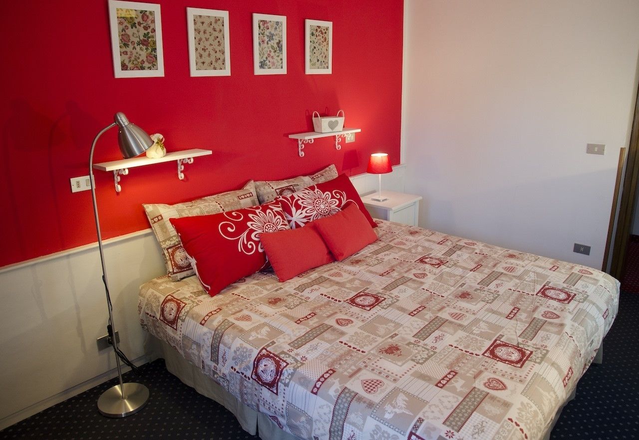 A bedroom with a red wall, a patterned bedspread, and a bedside lamp.