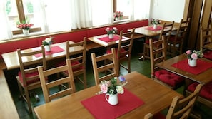 En matplats med bord och stolar i trä, röda kuddar och blomvaser på varje bord.