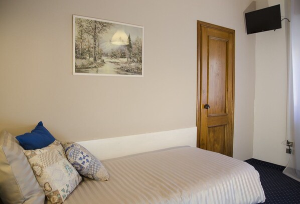 A bedroom with a bed, pillows, a painting, a wooden door, and a TV mounted on the wall. - Albergo al Sole Zoldo Alto (Val di Zoldo)