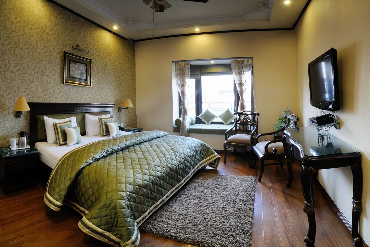 A hotel room with a bed, a desk, a chair, a television, and a window with curtains.