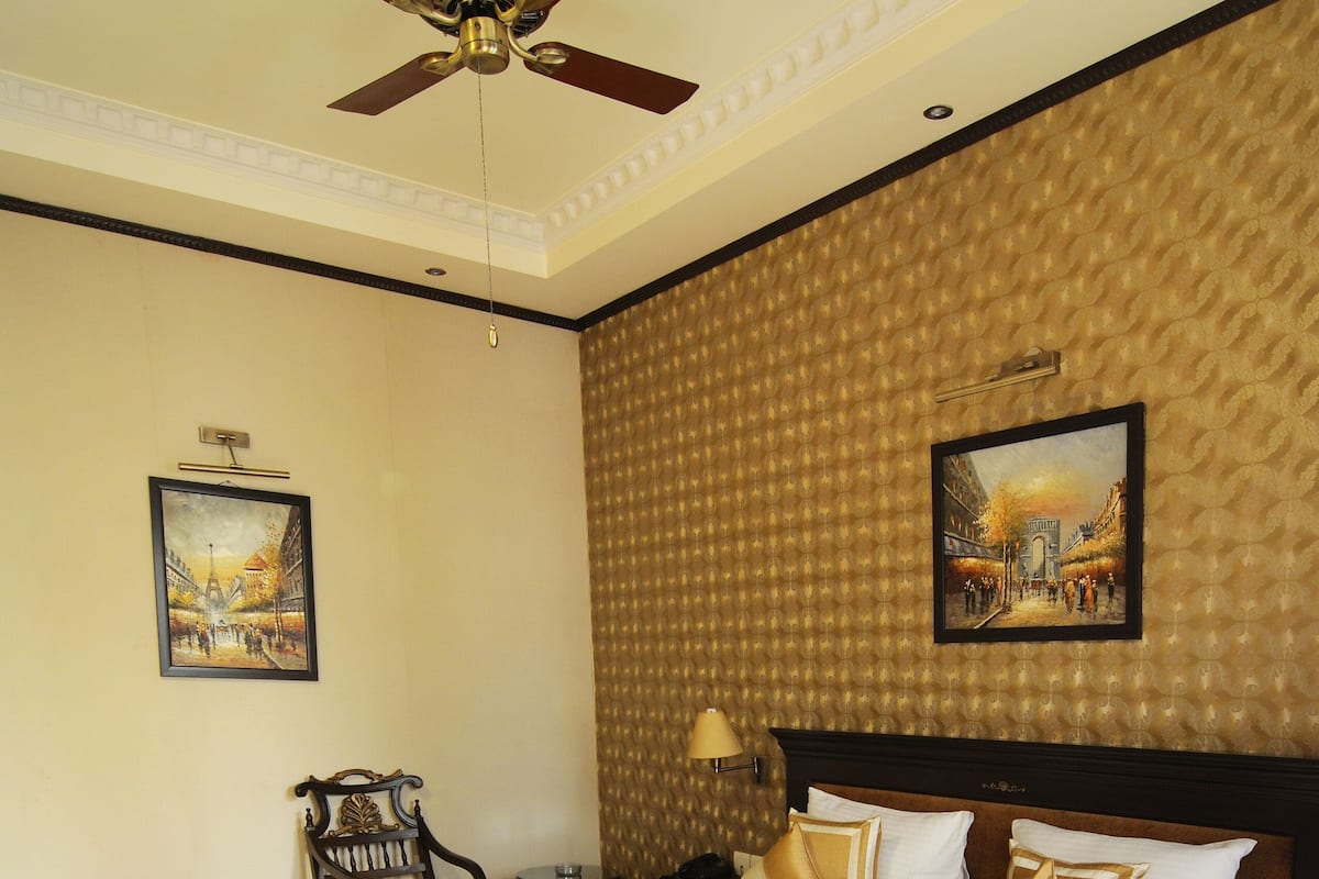 A hotel room with a large bed, a ceiling fan, a wooden floor, and a wall with a textured pattern.