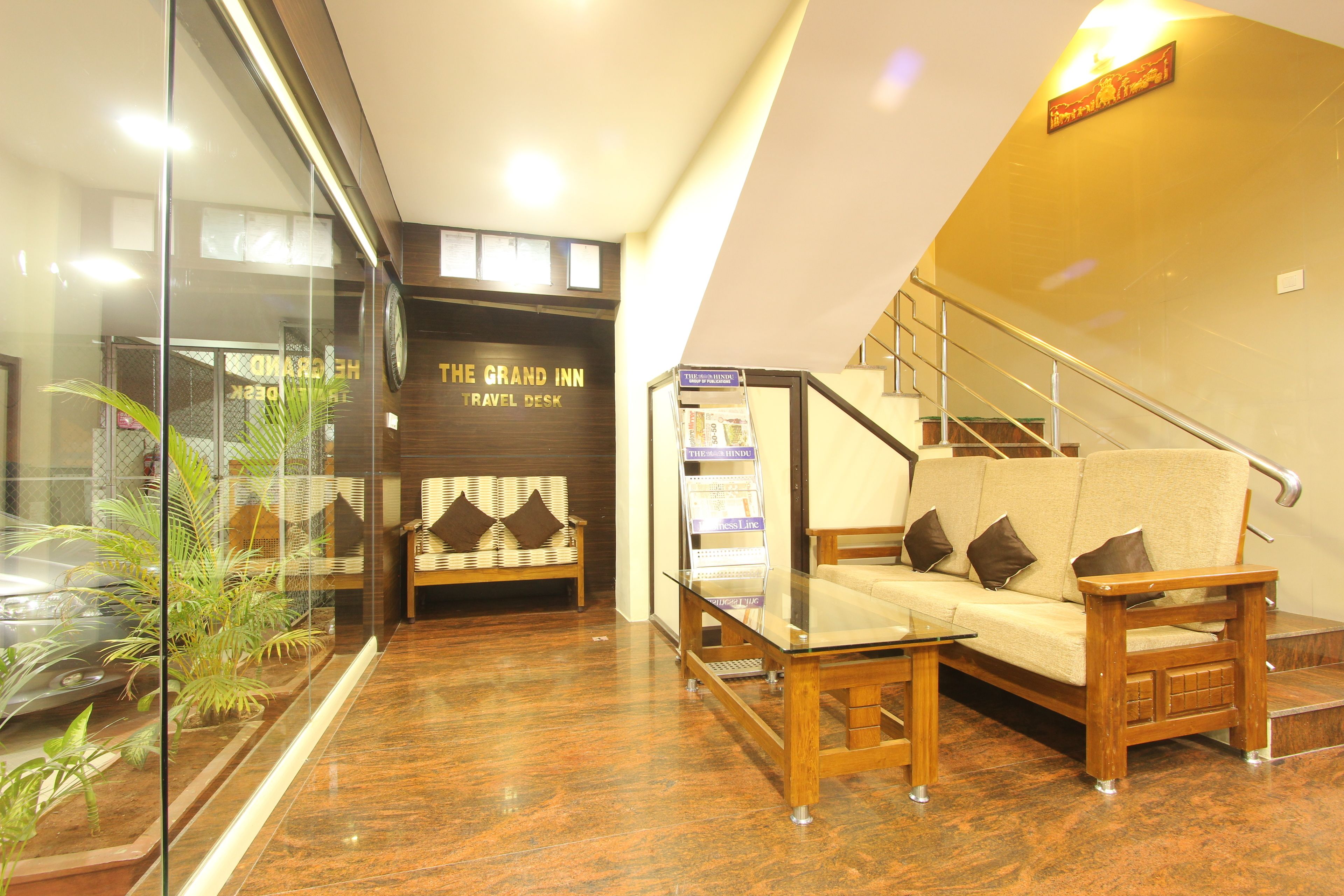 A lobby with a reception desk, a sofa, a staircase, and a glass partition with plants.