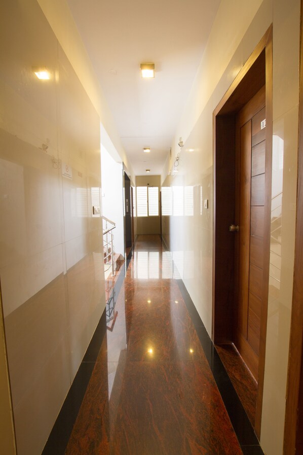 Un pasillo con piso pulido, una puerta de madera y una escalera con barandilla de metal.