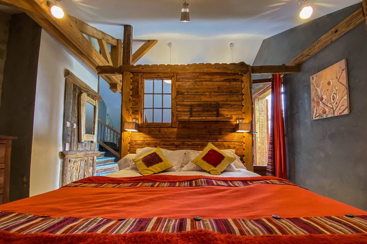 A cozy log cabin-style bedroom with a large bed, wooden beams, and a window.
