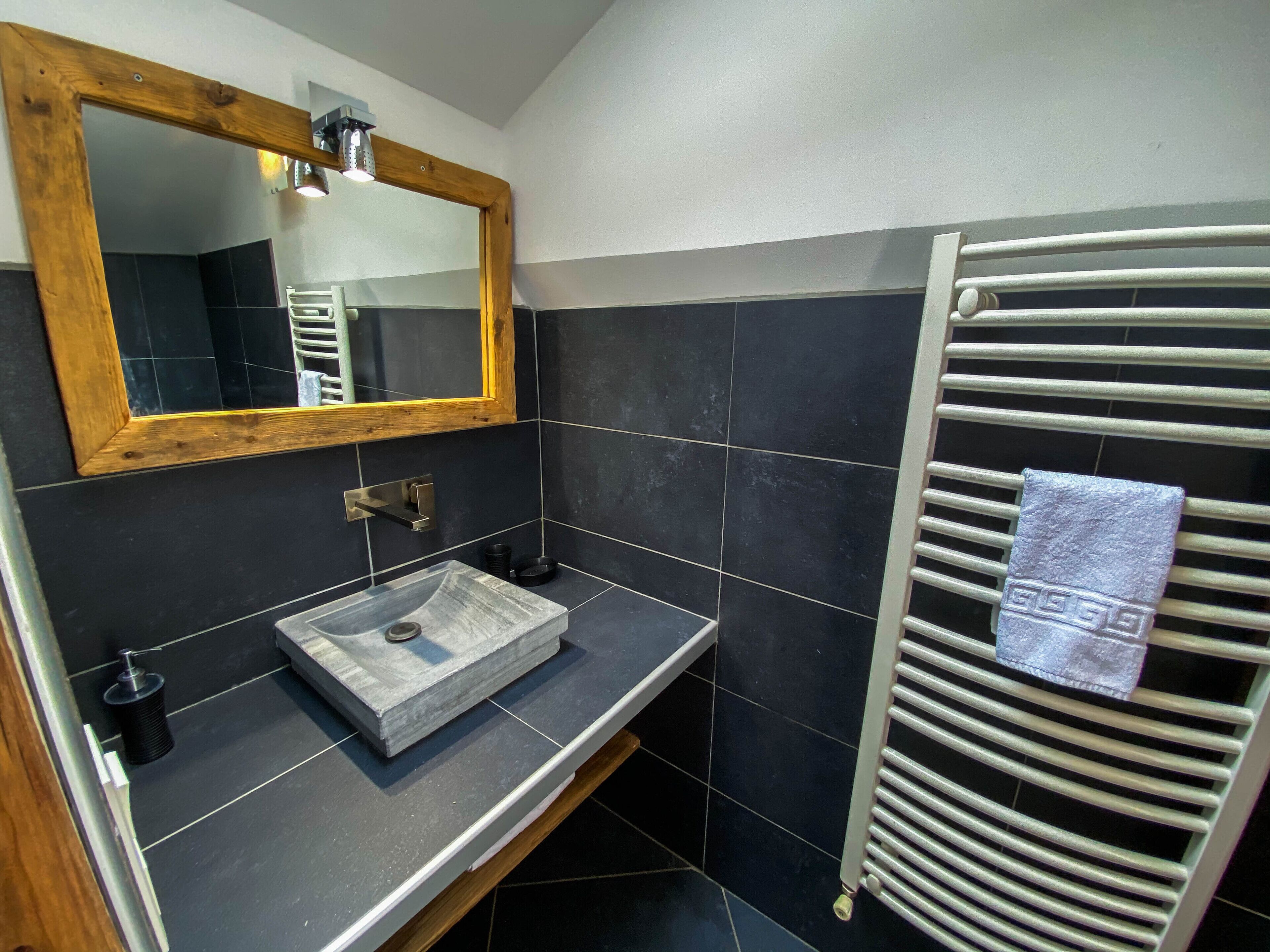 A bathroom with a wooden-framed mirror, a vessel sink, and a towel rack with a towel.