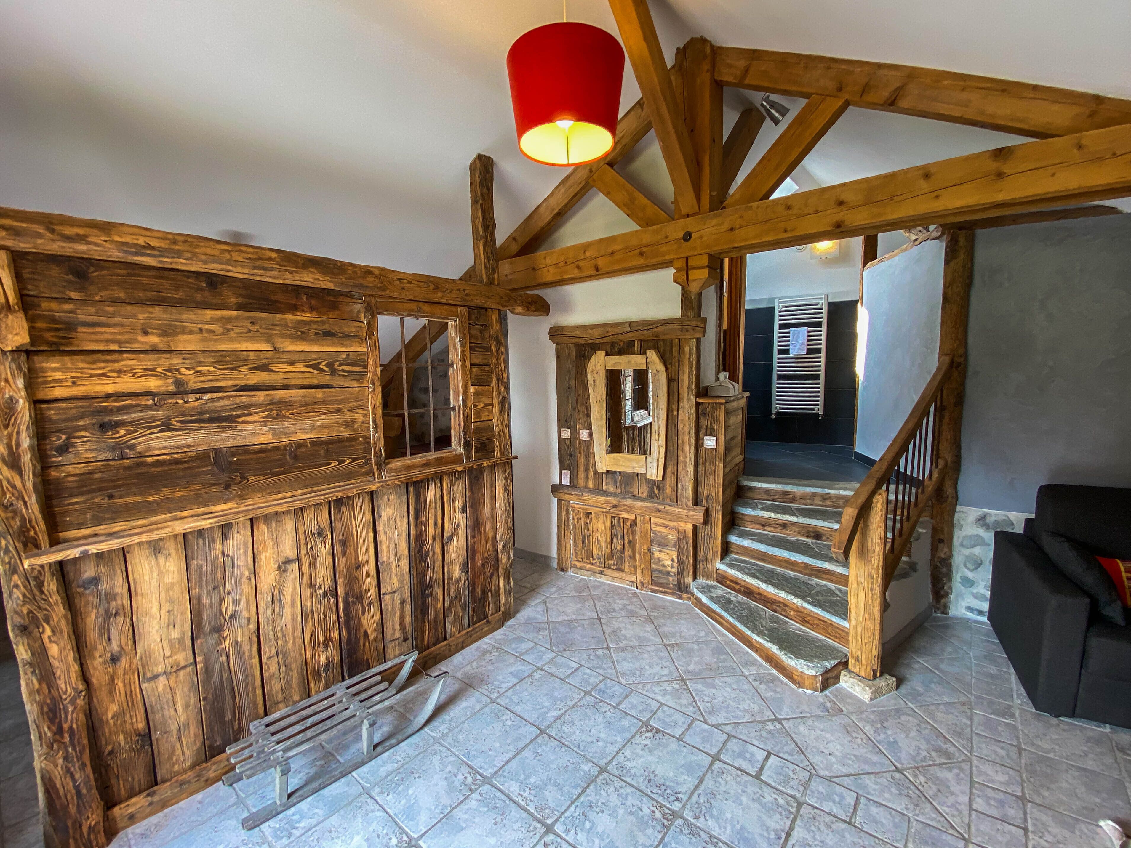 A rustic interior with wooden walls, a stone staircase, and a red hanging light fixture.