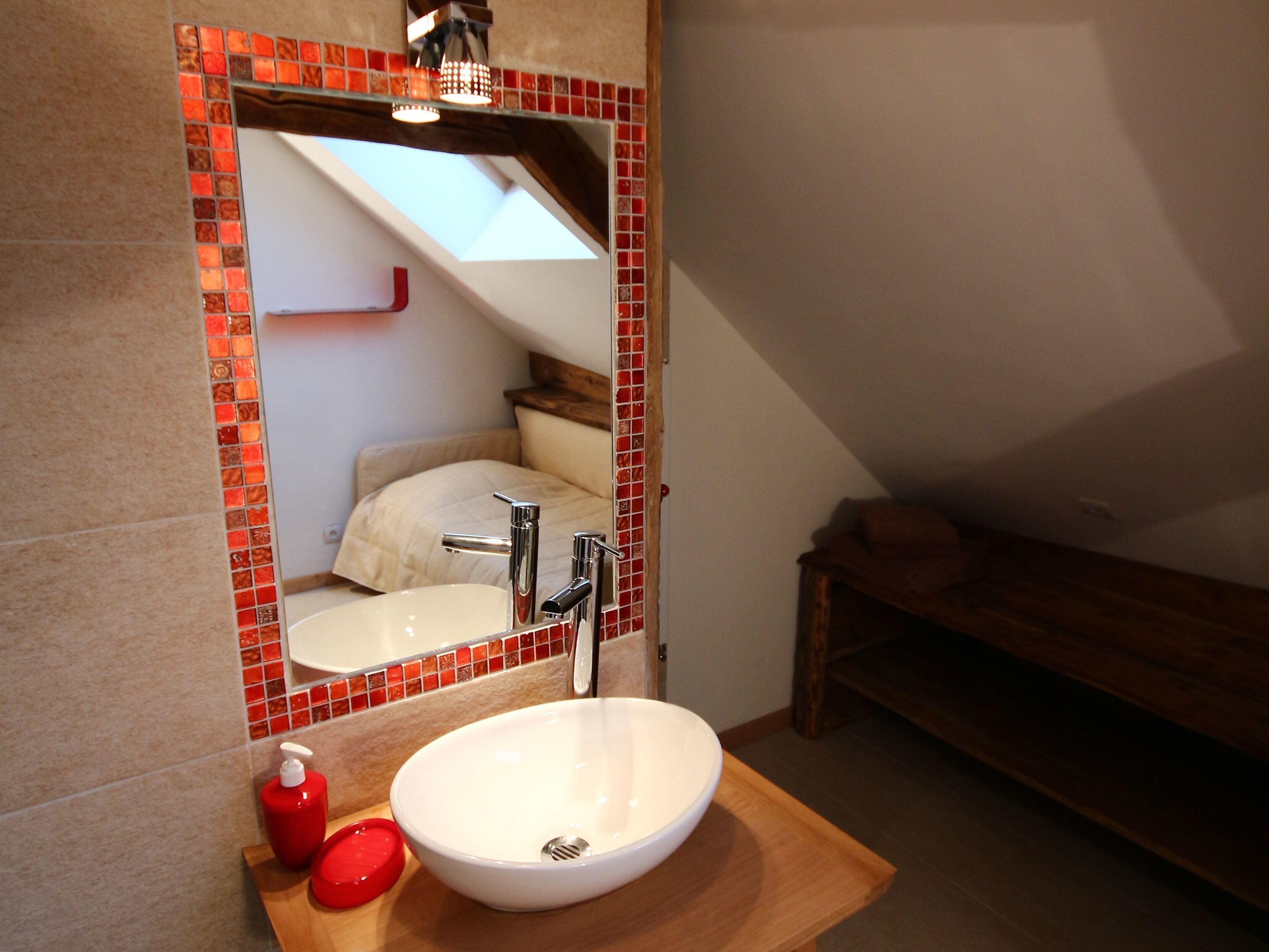 A bathroom with a white sink, red soap dispenser, and a mirror with a red frame.