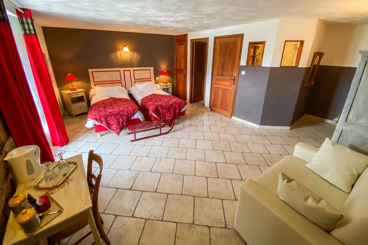 A room with two beds, a wooden rocking chair, a small table with a tray, and a couch.