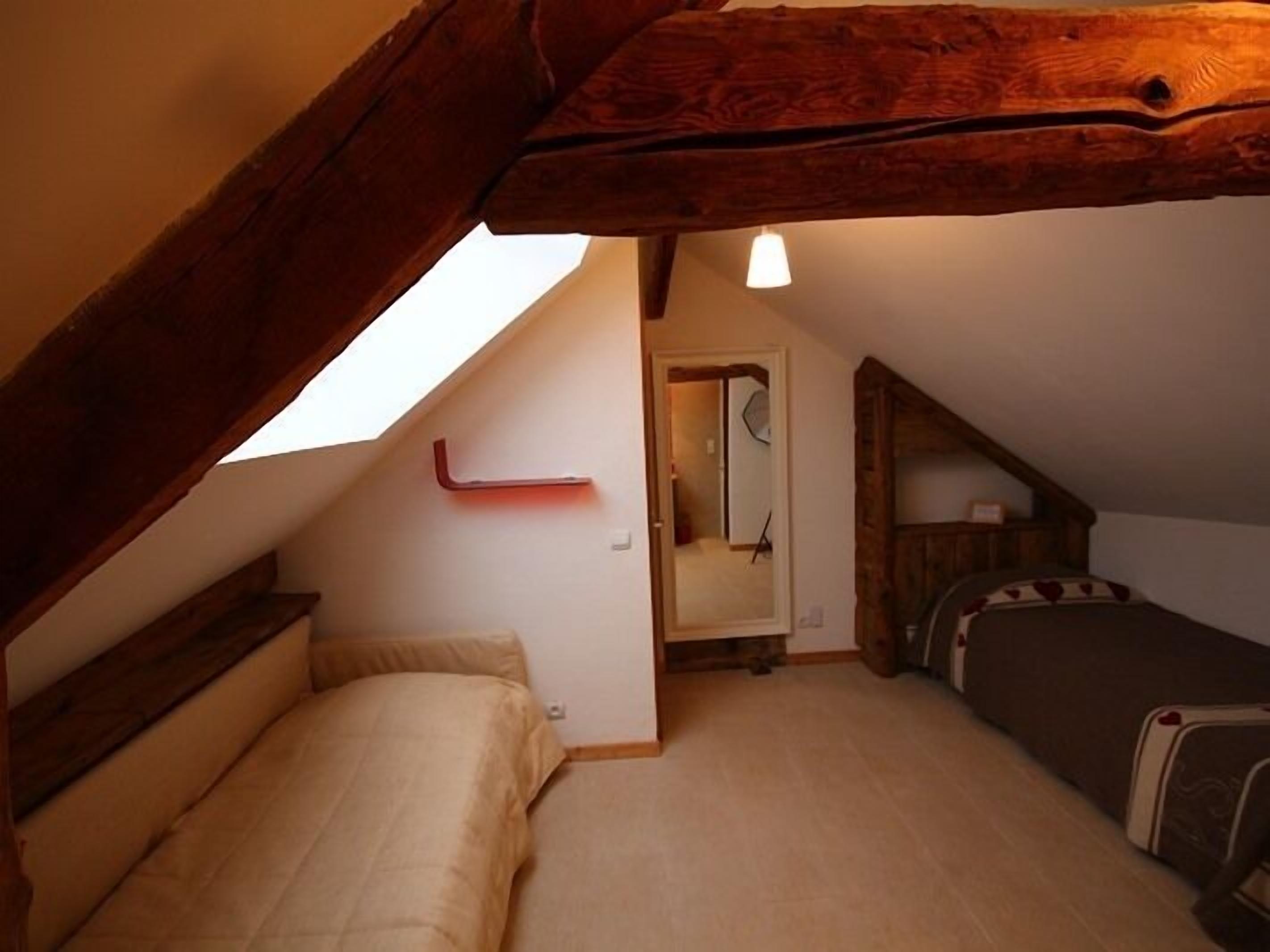 A small, cozy attic bedroom with a sloped ceiling, a single bed, and a small table.