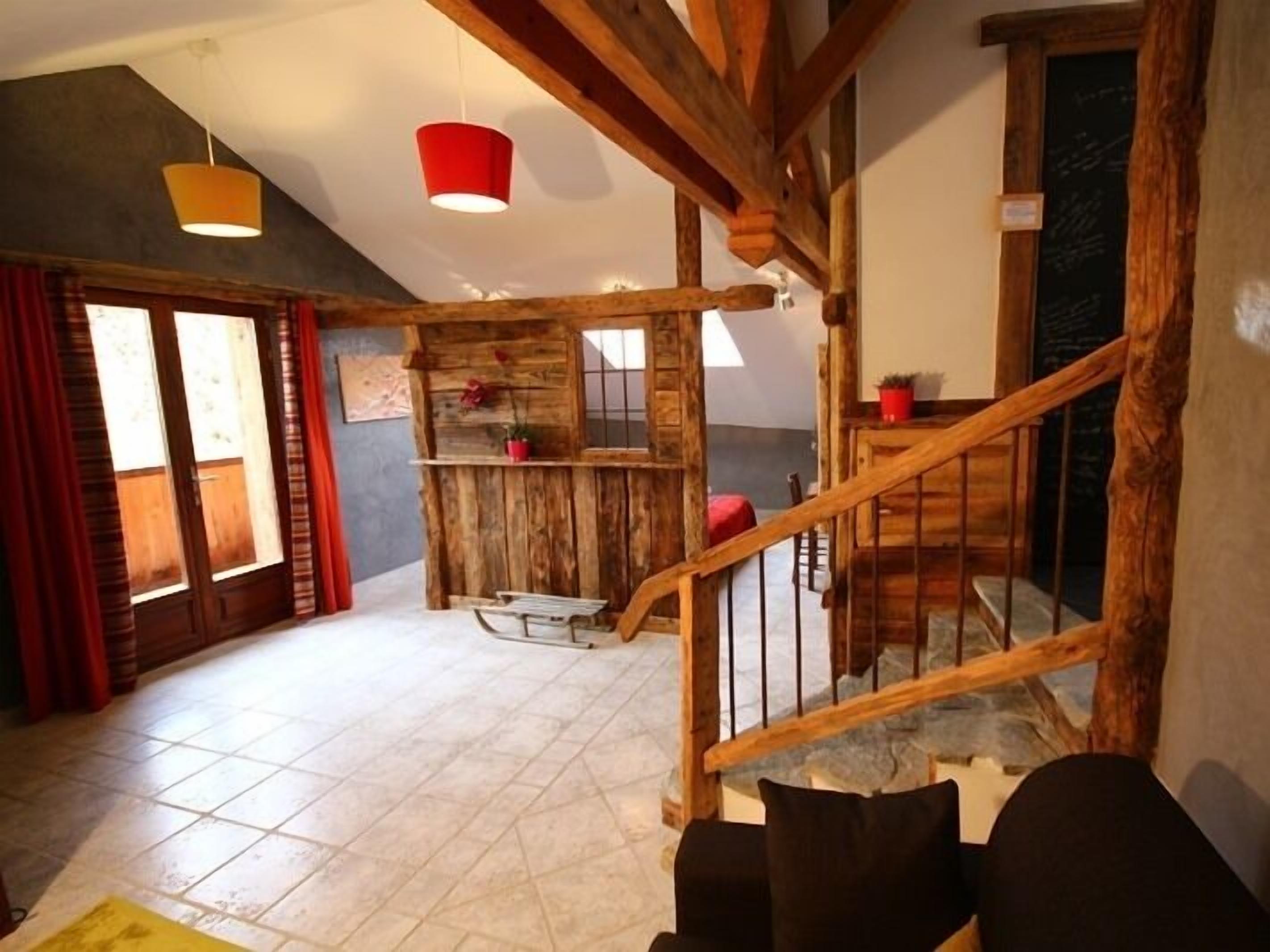 A rustic interior with a wooden staircase, a red hanging light, and a tiled floor.