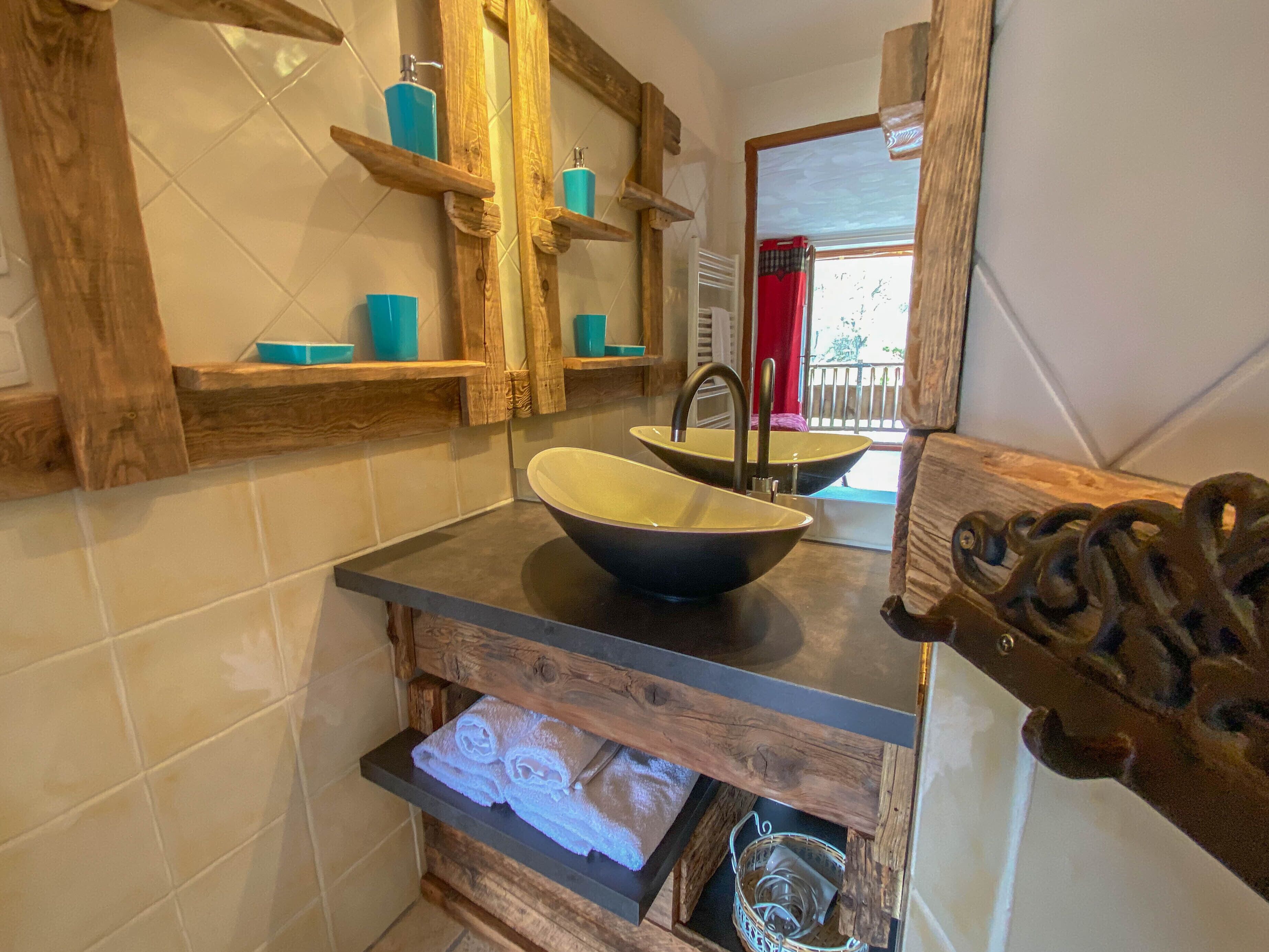 Une salle de bain avec un meuble-lavabo en bois, un grand évier et des étagères où sont rangés les produits de toilette.