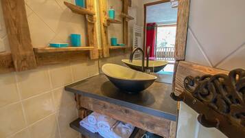 Une salle de bain avec un meuble-lavabo en bois, un grand évier et des étagères où sont rangés les produits de toilette.