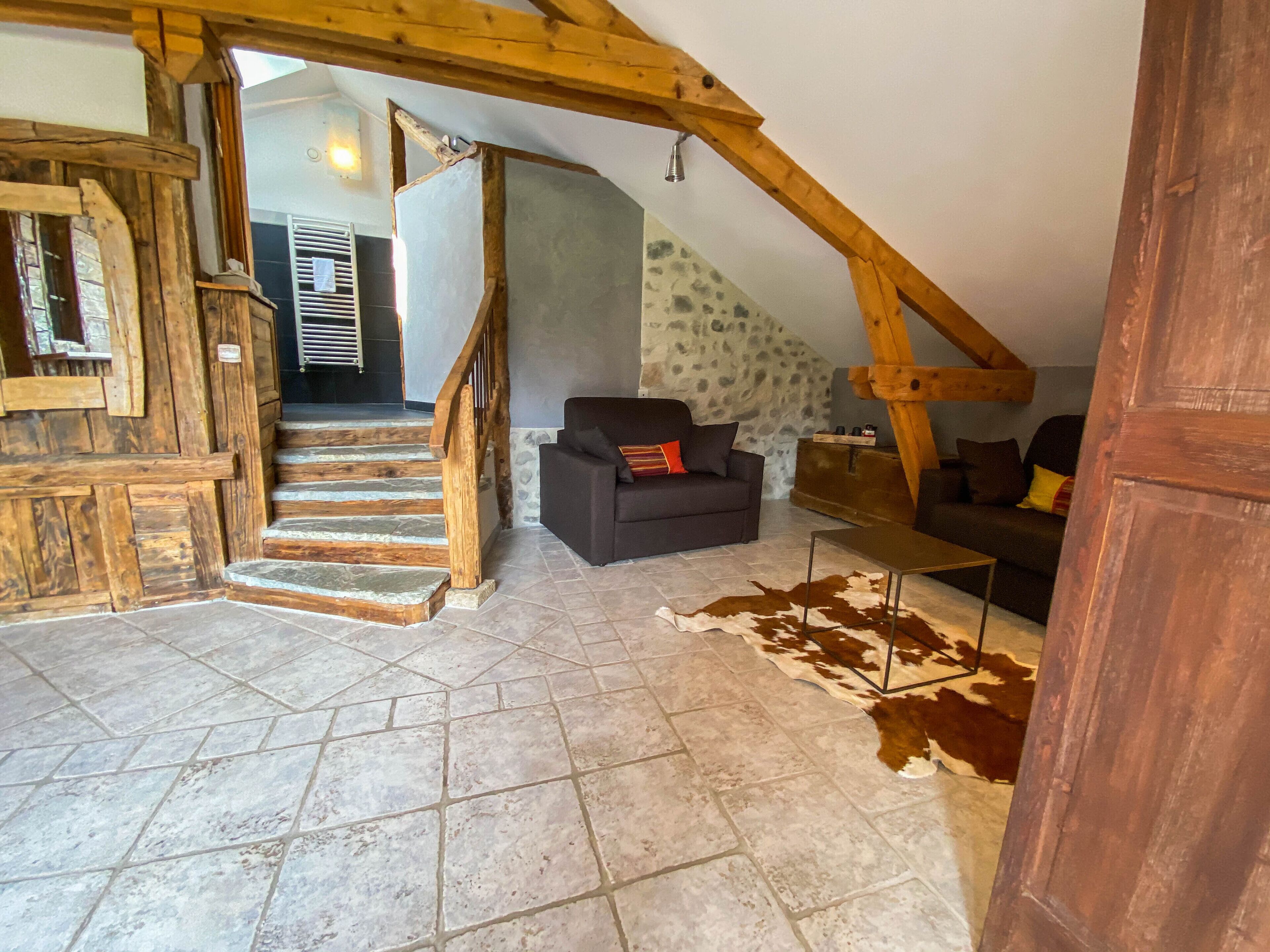 A rustic interior with a stone staircase, wooden beams, a sofa, and a cowhide rug.