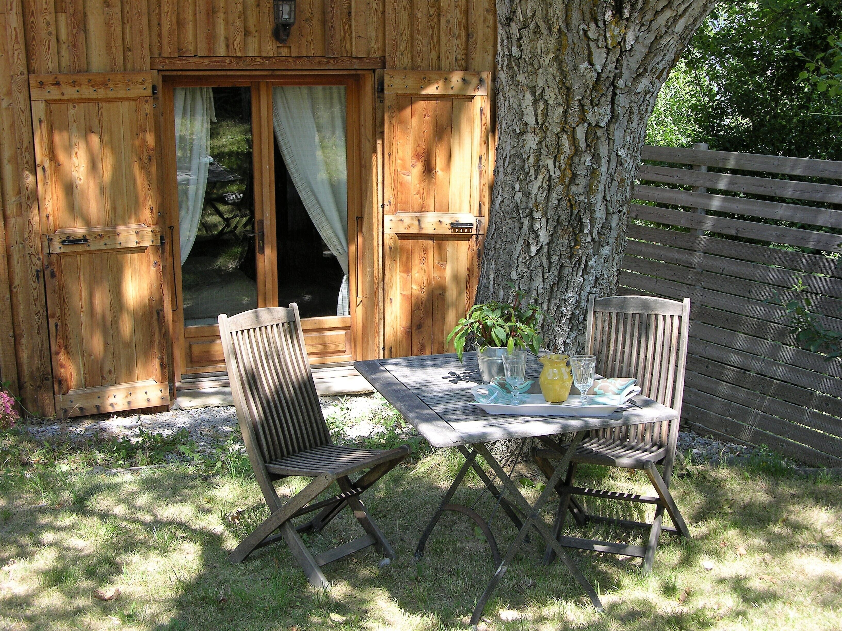 Una mesa de madera al aire libre con dos sillas, una planta en maceta y una jarra de agua.