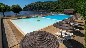 A swimming pool with lounge chairs and umbrellas, surrounded by a forested hillside. - Camping le Gibanel (Saint Martial Entraygues)