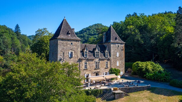 A historic stone building with multiple towers and a courtyard with outdoor seating. - Camping le Gibanel (Saint Martial Entraygues)