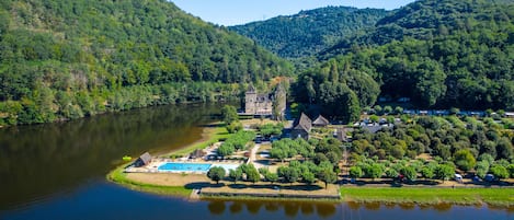 Un complexe hôtelier au bord d’un lac, doté d’une piscine, d’un grand bâtiment en pierre et entouré de verdure.