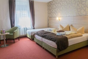 A hotel room with two beds, a green armchair, a small table, and a patterned wall. - Hotel Zur Post (Wurzen)