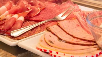 Una variedad de embutidos en un plato, incluyendo jamón y salami, con un tenedor y un bol de vidrio cerca.