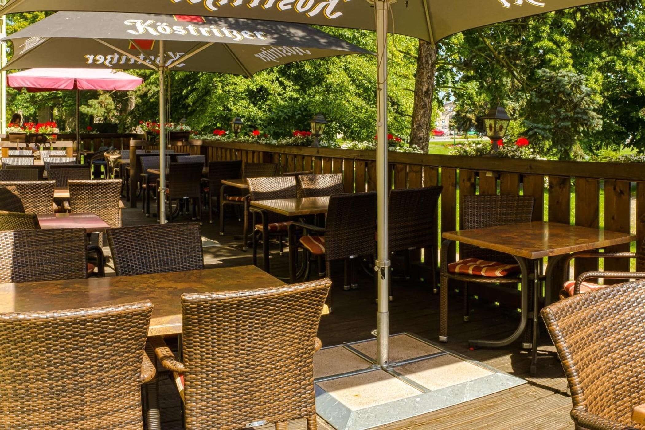 Ein Café im Freien mit Korbmöbeln und Sonnenschirmen, umgeben von viel Grün.