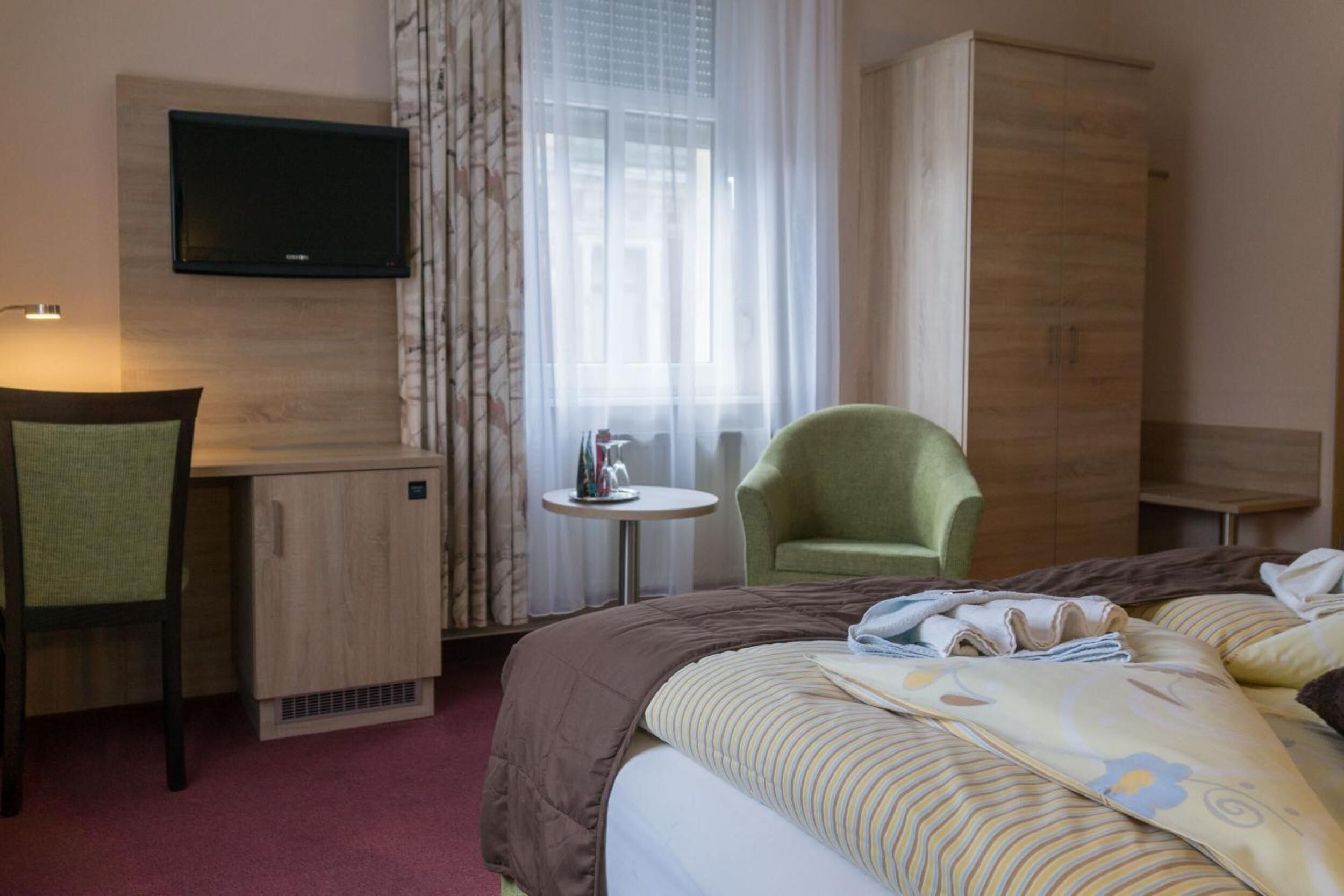 Een hotelkamer met een bed, een bureau, een stoel, een televisie, een kledingkast en een raam met gordijnen.