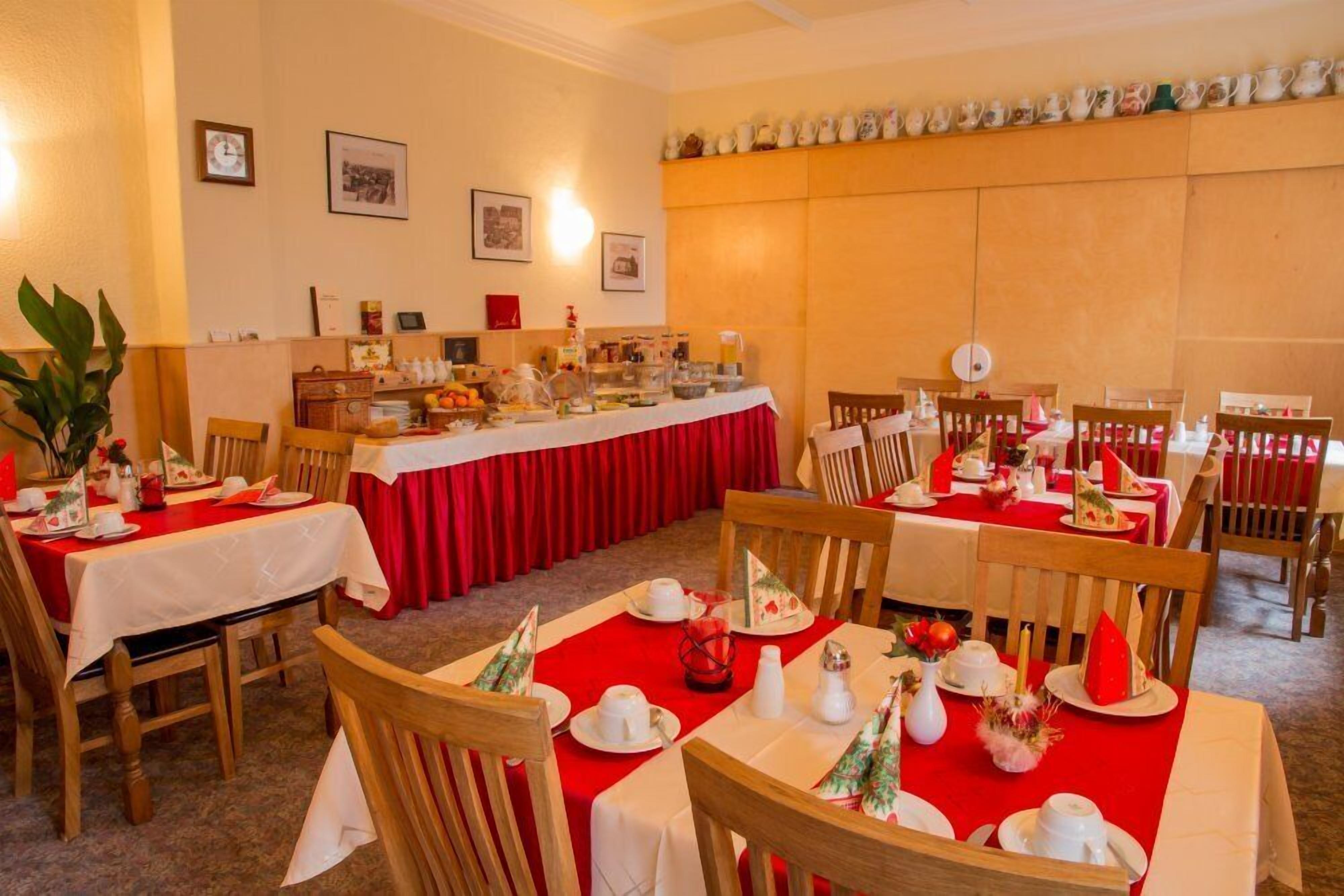Comedor con mesas dispuestas para una comida, con manteles rojos y platos blancos.