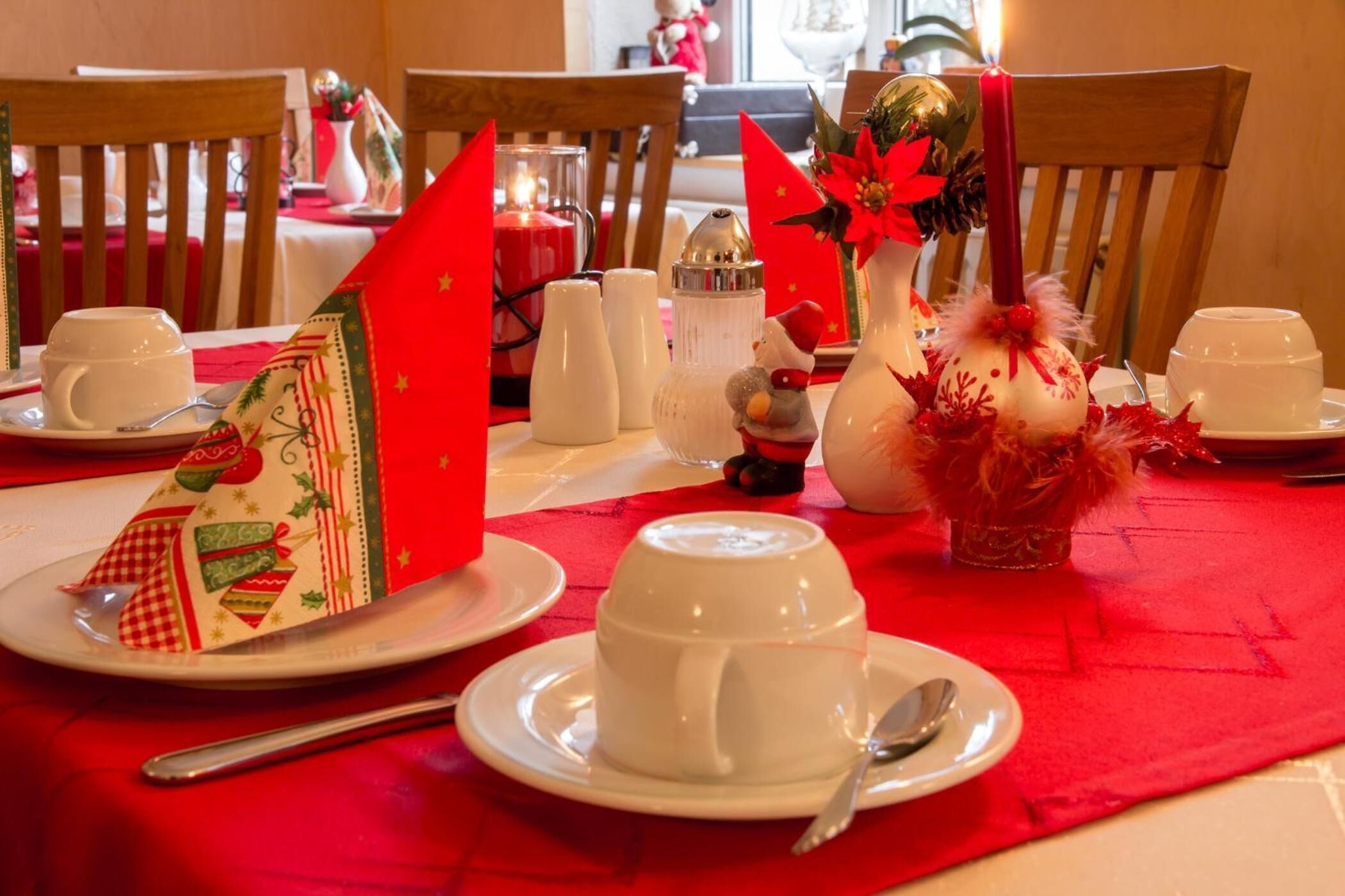 Una mesa de comedor con tazas, platillos blancos y un mantel rojo.