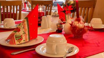 Una mesa de comedor con tazas, platillos blancos y un mantel rojo.