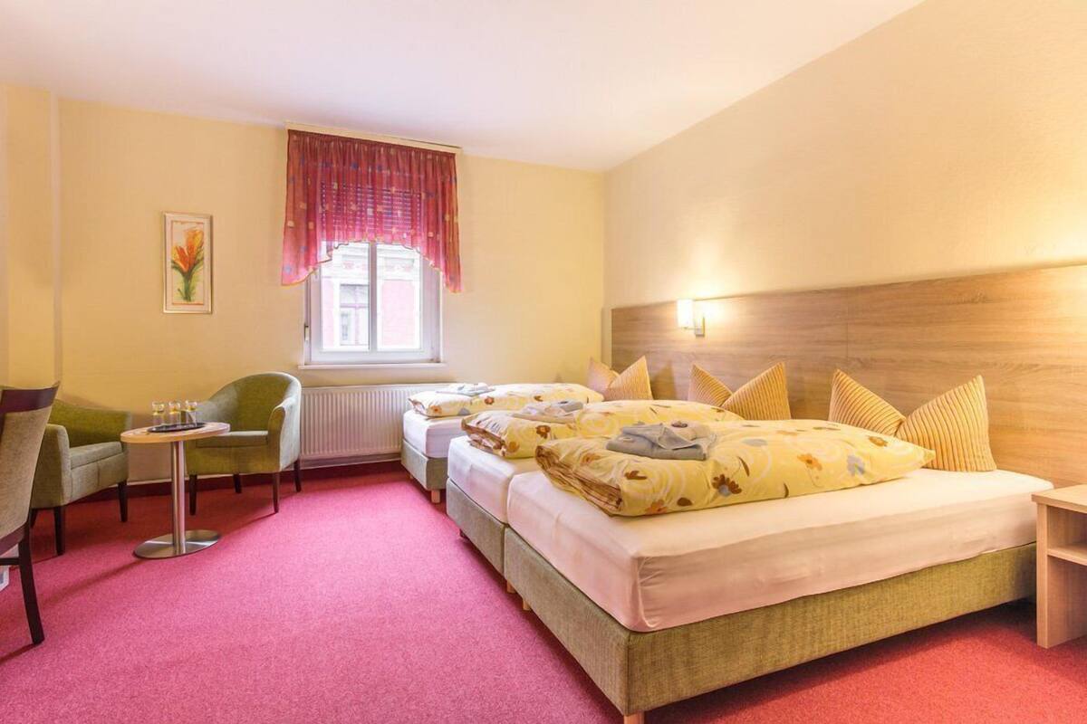 A hotel room with two beds, a small table with drinks, a chair, and a window with curtains.