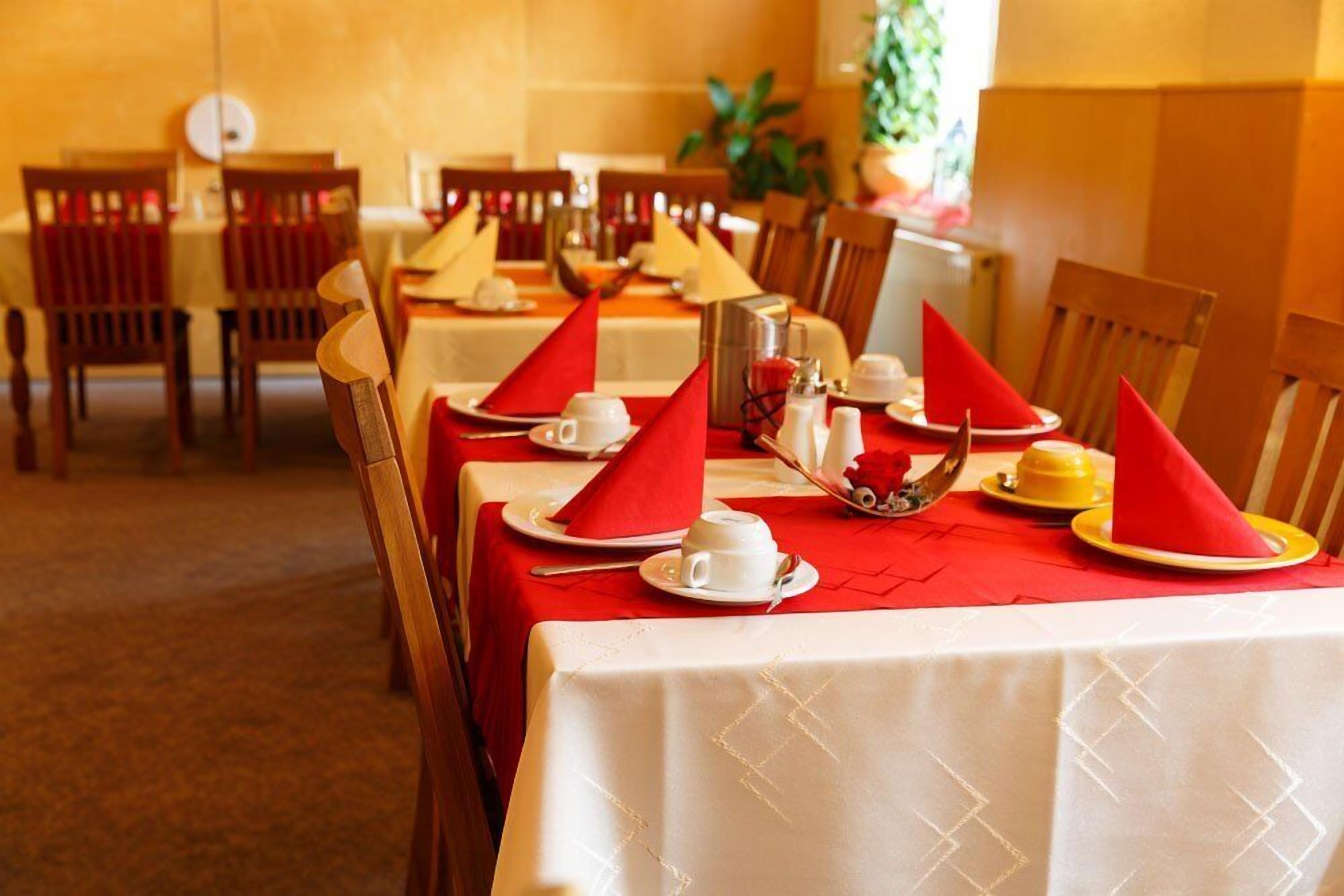 A dining area with tables set with red napkins, white tablecloths, and a variety of tableware.