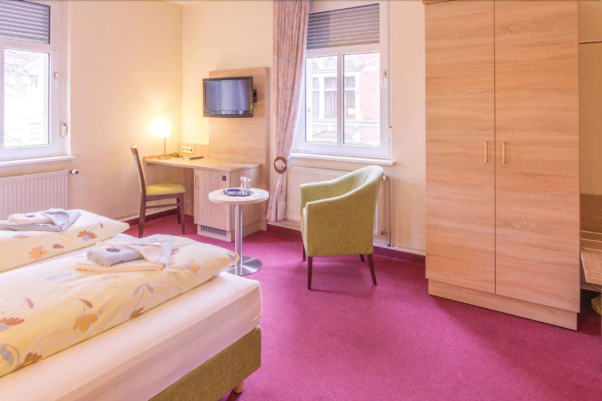 A hotel room with two beds, a desk, a chair, a television, and a wardrobe.